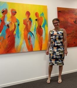Kunstner Tine Weppler står på en kunstudstilling foran hendes flotte store farverige malerier